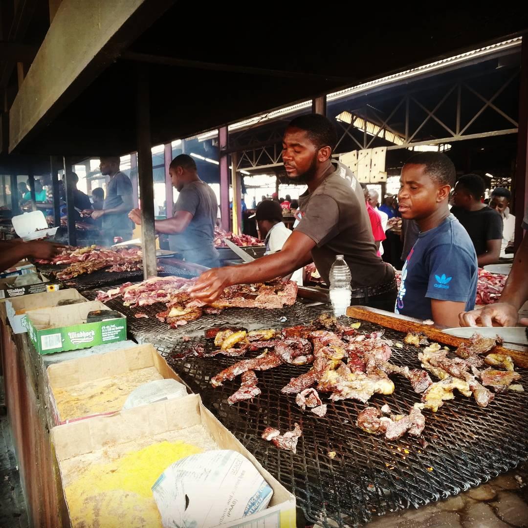 Cooks tending meat on grills at an open-sided market stall